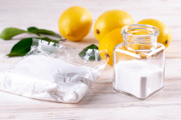 A jar of white salt and fresh lemons placed on a wooden surface, showcasing natural cleaning ingredients.