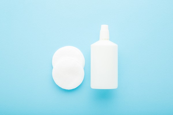 A bottle ofHydrogen Peroxide a spray nozzle and two cotton pads on a soft blue background.