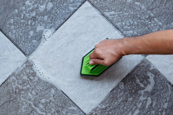 Person scrubbing a tile with a green scrubber and foam.