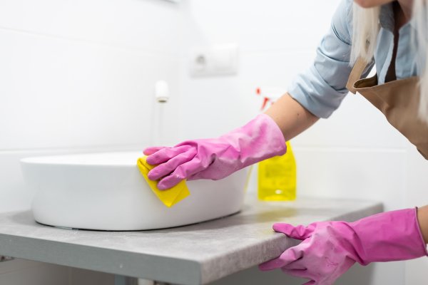 Person wearing pink gloves cleaning a white sink with a yellow cloth.